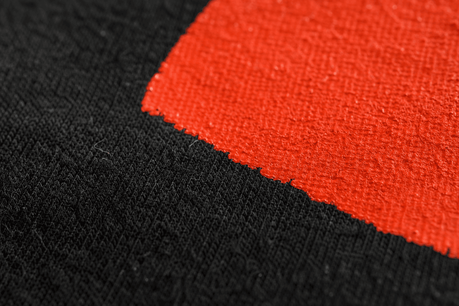 Macro d'une impression orange sur coton noir, le tissage est visible